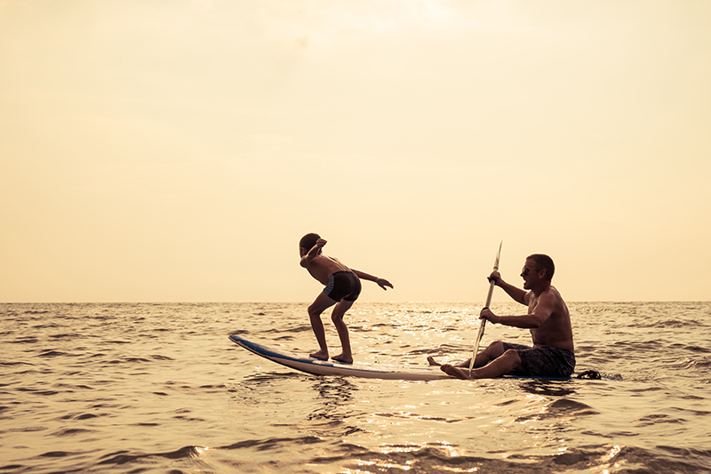 Father and baby son playing on the beach at the day time. People having fun outdoors. Concept of summer vacation and friendly family.